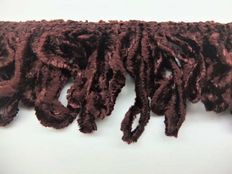 May include: A close-up of a brown velvet fringe trim. The fringe is made of soft, fluffy fibers and has a slightly textured appearance.