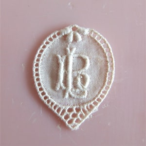 Puede incluir: Círculo de encaje blanco bordado con la letra "IB" en el centro.