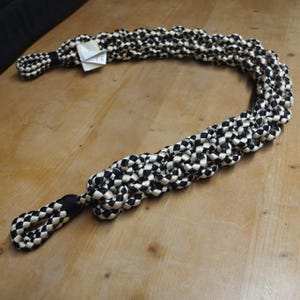 May include: A black and cream-colored braided rope leash. The leash is made of tightly woven rope, with a checkerboard pattern. The leash has a loop at each end. A small tag is attached to the leash.