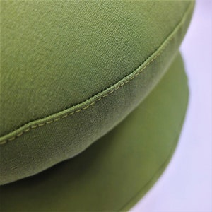 May include: A close-up of a green fabric cushion with a stitched seam. The cushion is round and has a soft, textured surface.