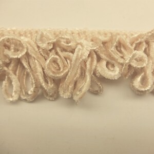 May include: Cream-colored fabric trim with a curly, looped fringe. The trim is soft and fluffy, and would be perfect for adding a touch of elegance to any project.
