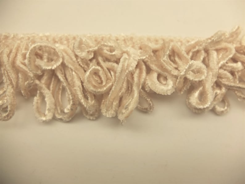 May include: Cream-colored fabric trim with a curly, looped fringe. The trim is soft and fluffy, and would be perfect for adding a touch of elegance to any project.