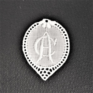 Pode incluir: Tecido branco bordado com uma borda festonada e a letra "A" no centro.
