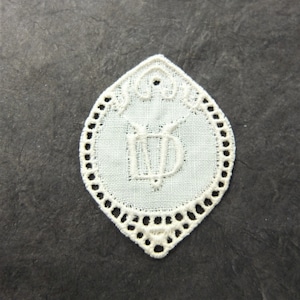 Könnte beinhalten: Weiße Spitzentischdecke mit einem gewellten Rand und einem Monogramm "MD" in der Mitte.