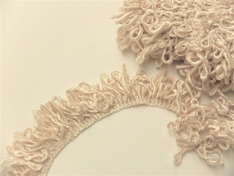 May include: Cream-colored fabric trim with a fringe design. The trim is made of soft, looped fabric and has a delicate, feminine look.