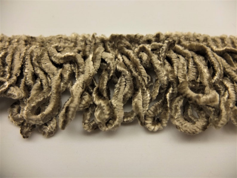 May include: A close-up of a beige velvet trim with a fringe texture. The trim is made of soft, curly fibers.