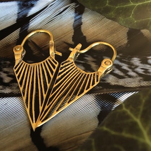 May include: A pair of gold-toned geometric earrings with a triangular shape and a fan-like design. The earrings are on a background of black and white feathers.