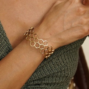 May include: Gold honeycomb-shaped bracelet. The bracelet is made of metal and has a delicate, openwork design.
