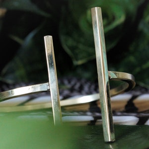 May include: A gold metal bangle bracelet with two vertical bars. The bracelet is on a patterned surface.