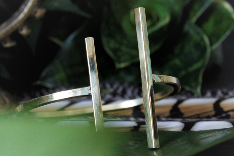 May include: A gold metal bangle bracelet with two vertical bars. The bracelet is on a patterned surface.