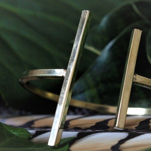 May include: A gold-toned metal ring with a thick, straight bar design. The ring is open and adjustable.
