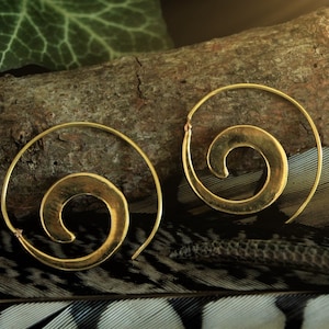 May include: A pair of gold-toned hoop earrings with a spiral design. The earrings are on a wooden surface with a feather background.