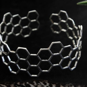 May include: A silver bracelet with a honeycomb design. The bracelet is open and has a simple, modern style.