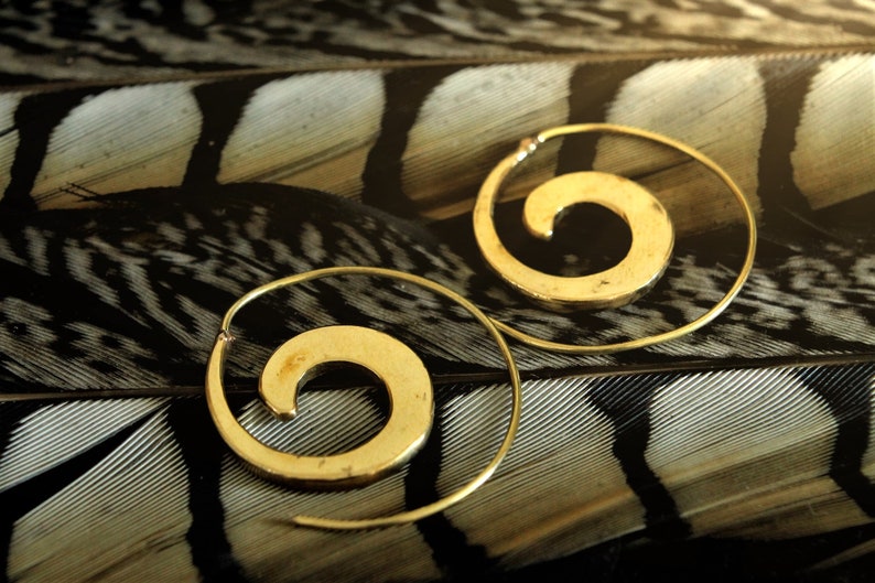 May include: A pair of gold hoop earrings with a spiral design. The earrings are on a black and white patterned background.