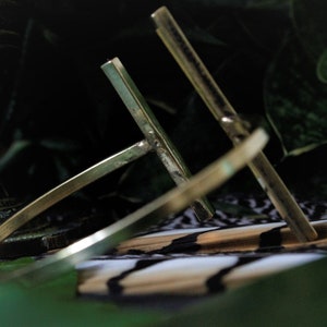 May include: A gold-toned metal bracelet with a simple, geometric design. The bracelet is made of two intersecting bars, creating a cross shape.