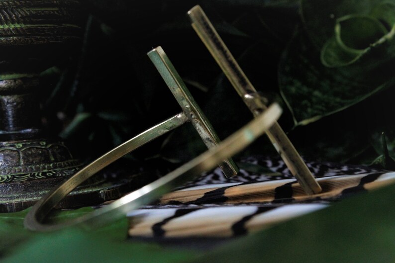 May include: A gold-toned metal bracelet with a simple, geometric design. The bracelet is made of two intersecting bars, creating a cross shape.