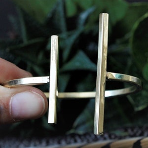 May include: A gold-toned metal bracelet with two vertical bars. The bracelet is open and adjustable.