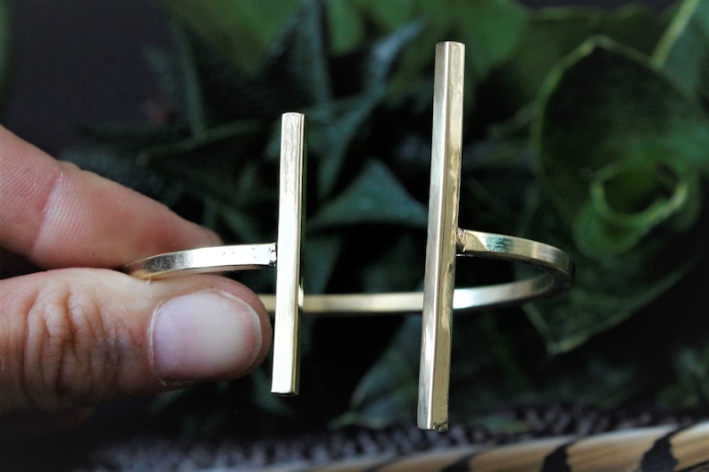 May include: A gold-toned metal bracelet with two vertical bars. The bracelet is open and adjustable.