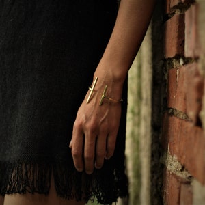 May include: A gold metal bracelet with a simple, minimalist design. The bracelet is made of two thin, straight bars that intersect at a right angle.