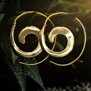 May include: A pair of gold-toned hoop earrings with a spiral design. The earrings are made of metal and have a hammered finish.