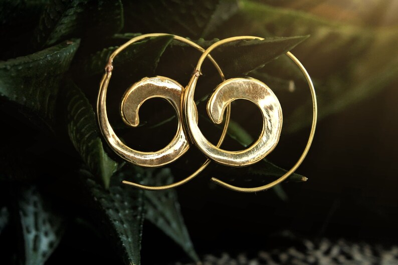 May include: A pair of gold-toned hoop earrings with a spiral design. The earrings are made of metal and have a hammered finish.
