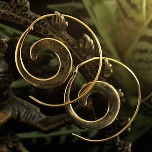 Puede incluir: Un par de pendientes de aro dorados con un diseño en espiral. Los pendientes están hechos de metal y tienen un acabado brillante.