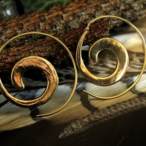 May include: A pair of gold-toned spiral hoop earrings. The earrings are made of a hammered metal and have a textured finish.