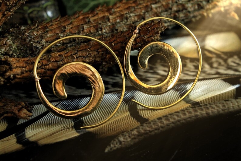 May include: A pair of gold-toned spiral hoop earrings. The earrings are made of a hammered metal and have a textured finish.