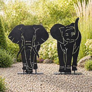 Puede incluir: Dos esculturas de elefantes de metal negro con detalles dorados se alzan sobre un camino de grava en un jardín. Un elefante tiene la trompa levantada. Arte decorativo para jardín.