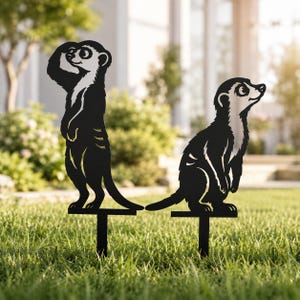 May include: Two black metal meerkat silhouettes designed as garden stakes. One meerkat stands upright with a paw near its head, while the other sits in a watchful pose. Both figures feature cut-out details and are mounted on thin metal spikes.
