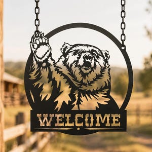 May include: Black metal bear sign with the word "WELCOME" in gold lettering. The bear is inside a black circle and is raising its paw. The sign hangs from two chains.