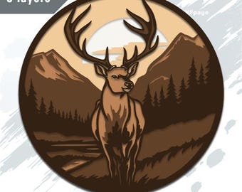 May include: A layered, circular design featuring a deer with large antlers set against a mountain and forest backdrop. The color palette includes shades of brown and tan, with the text "5 layers" in the upper left corner and "SVG DXF EPS" at the bottom.