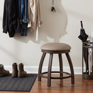 May include: A home entryway with a wooden coat rack holding a black jacket, denim jacket, and beige coat. A round stool with a brown frame and tan seat sits nearby. Boots and a doormat are on the floor.
