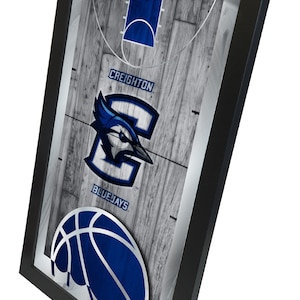 May include: A framed print of a basketball court with a blue and white Creighton Bluejays logo and a basketball. The text "BASKETBALL" is at the top of the image and "CREIGHTON" and "BLUEJAYS" are below the logo.