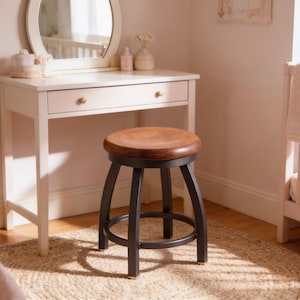 May include: A white vanity table with a round mirror and a wooden stool with a brown seat and black metal legs. The stool is in front of the vanity table. A crib and a rug are also in the room.