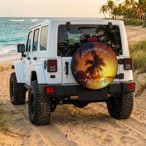 May include: A white Jeep Wrangler parked on a sandy beach, with a spare tire cover featuring a sunset palm tree design. The tire cover reads "Customizable Tire Cover". The ocean and palm trees are visible in the background.