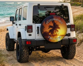 May include: A white Jeep Wrangler parked on a sandy beach, with a spare tire cover featuring a sunset palm tree design. The tire cover reads "Customizable Tire Cover". The ocean and palm trees are visible in the background.
