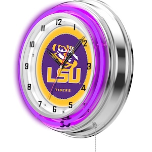 May include: A round, silver-colored neon clock with a purple neon ring. The clock face features the LSU Tigers logo in purple and gold. The clock has a pull chain and displays the time.