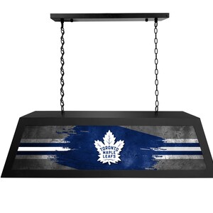 May include: Black hanging light fixture with a Toronto Maple Leafs logo on a blue and white distressed background.