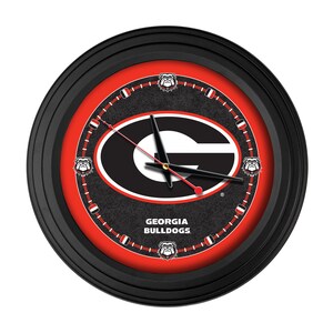 May include: Round black wall clock with a red and black face featuring the Georgia Bulldogs logo. The clock has a black outer rim and a red inner ring. The clock hands are black with a red second hand. The words "GEORGIA BULLDOGS" are printed on the face.