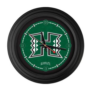May include: Round black wall clock with a green face featuring a white and green "H" logo and the word "HAWAII" at the bottom. The clock has black hands and white numbers at the 3, 6, 9, and 12 positions.