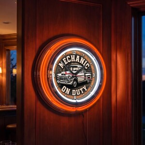 May include: A round wall clock with a bright orange neon ring border. The clock face features a vintage white pickup truck illustration in the center, surrounded by the text "MECHANIC ON DUTY" in bold black lettering, with black clock hands.