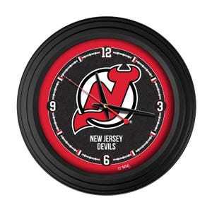 May include: A round black wall clock featuring the New Jersey Devils logo in red and white. The clock face has a black background with white numerals and a red inner ring. The hands are black and red.