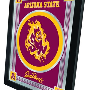 May include: A framed mirror with a silver background and a maroon border. The mirror features a gold circle with a cartoon devil holding a trident and flames. The text "Arizona State" and "Sun Devils" are also included in the design.