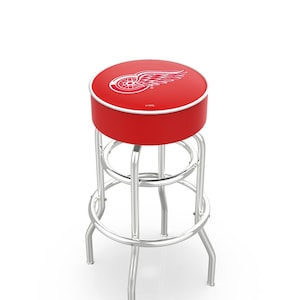 May include: A red bar stool with a chrome frame and a red cushioned seat featuring the Detroit Red Wings logo. The logo is a red and white winged wheel with the text "NHL" underneath.