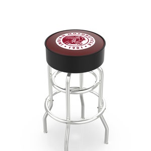 May include: A chrome-framed bar stool with a round, padded seat. The seat is burgundy with a black border and features the "Indian Motorcycle" logo in white. The stool has a footrest and four curved legs.