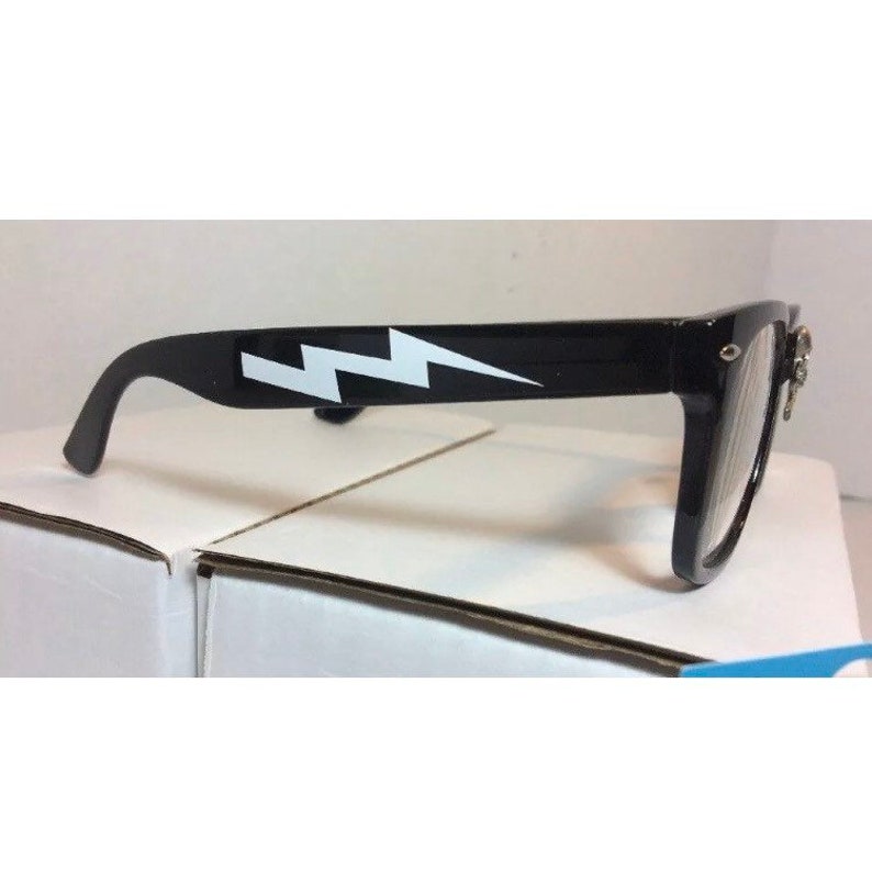 May include: Black plastic framed glasses with a white lightning bolt design on the side. The glasses have clear lenses.