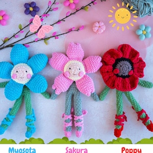 May include: Three handmade crochet flower dolls: Myosota (blue), Sakura (pink), and Poppy (red). Each doll has a smiling face, green stem-like legs, and ballet-style shoes. The background includes decorative flowers and a butterfly.