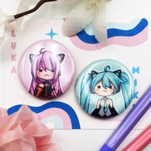 May include: Two round buttons with colorful anime characters. The left button is pink with a purple-haired character with cat ears. The right button is blue with a blue-haired character with cat ears. The text "LUKA" is on the left and "MIKU" is on the right.