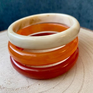 Könnte beinhalten: Drei übereinanderliegende Armreifen in Creme, Orange und Rot.